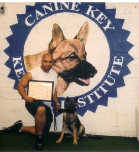 Don, proudly kneeling beside a graduated German Shepherd in front of the Canine Key Institute emblem, holding a certificate of completion